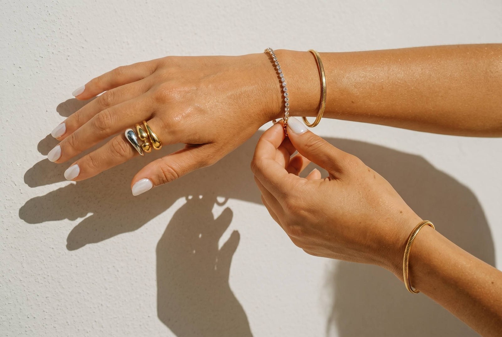 Close-up of hands wearing gold rings and bracelets on a light background